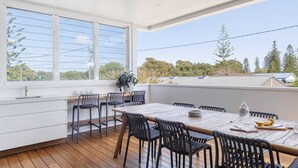 A modern kitchen with a wooden table and chairs, large windows, and a view of trees and buildings. - Sandhurst - Oceanstays (Yamba)