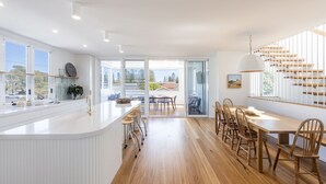A modern kitchen with a central island, wooden flooring, and large windows. - Sandhurst - Oceanstays (Yamba)