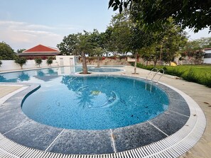 A circular swimming pool with a tiled edge, surrounded by a stone deck and trees. - Ganahera (Pushkar)