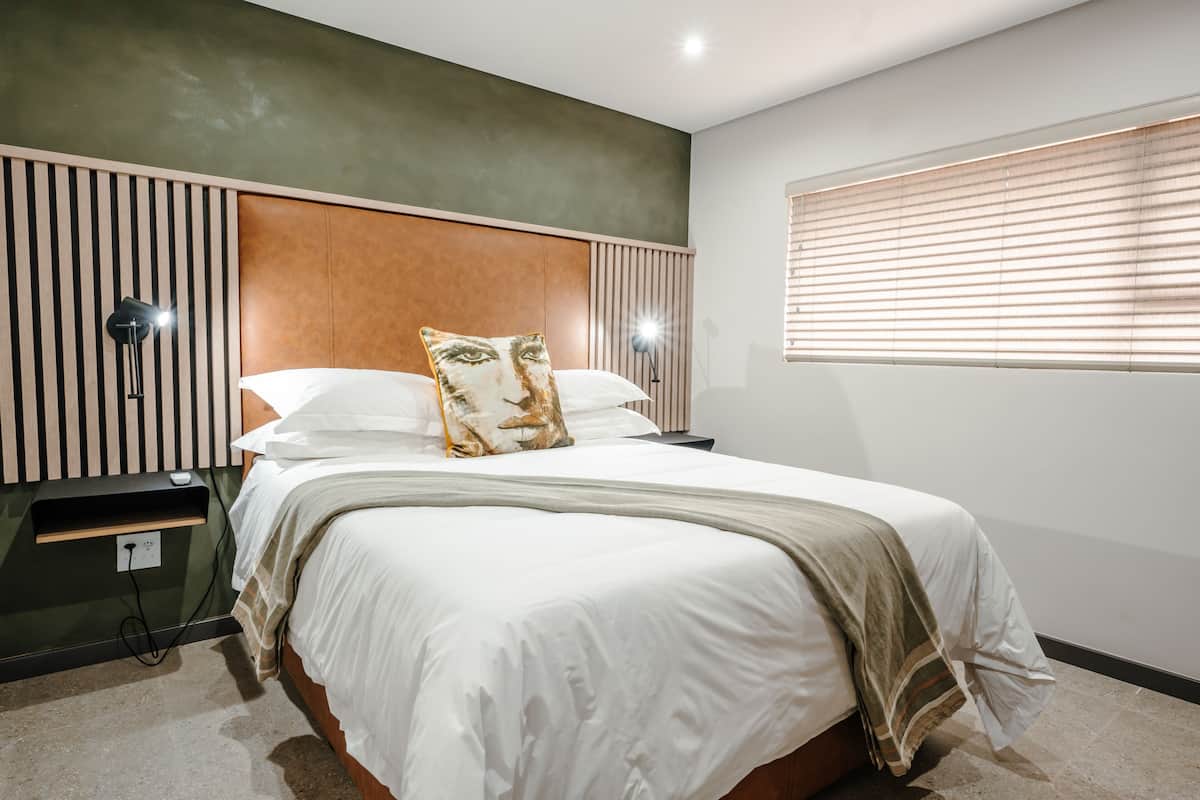 A neatly made bed with a pillow, a bedside lamp, and a power outlet on the wall.