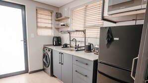 A compact kitchen with a washing machine, a sink, a coffee maker, and a refrigerator. - 80 on Thabo (Potchefstroom)