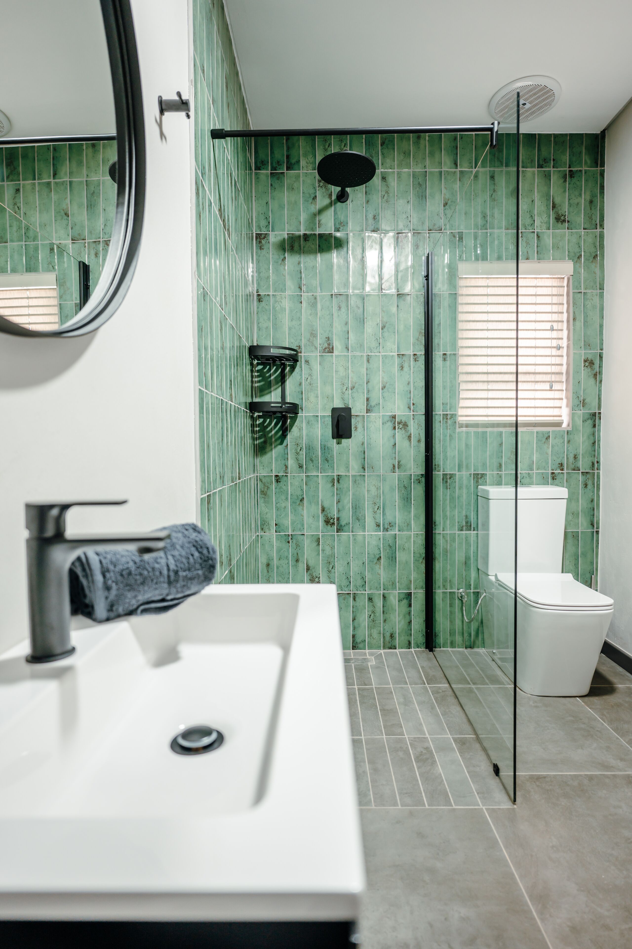Un baño con lavamanos blanco, espejo, ducha con puerta de vidrio y retrete.