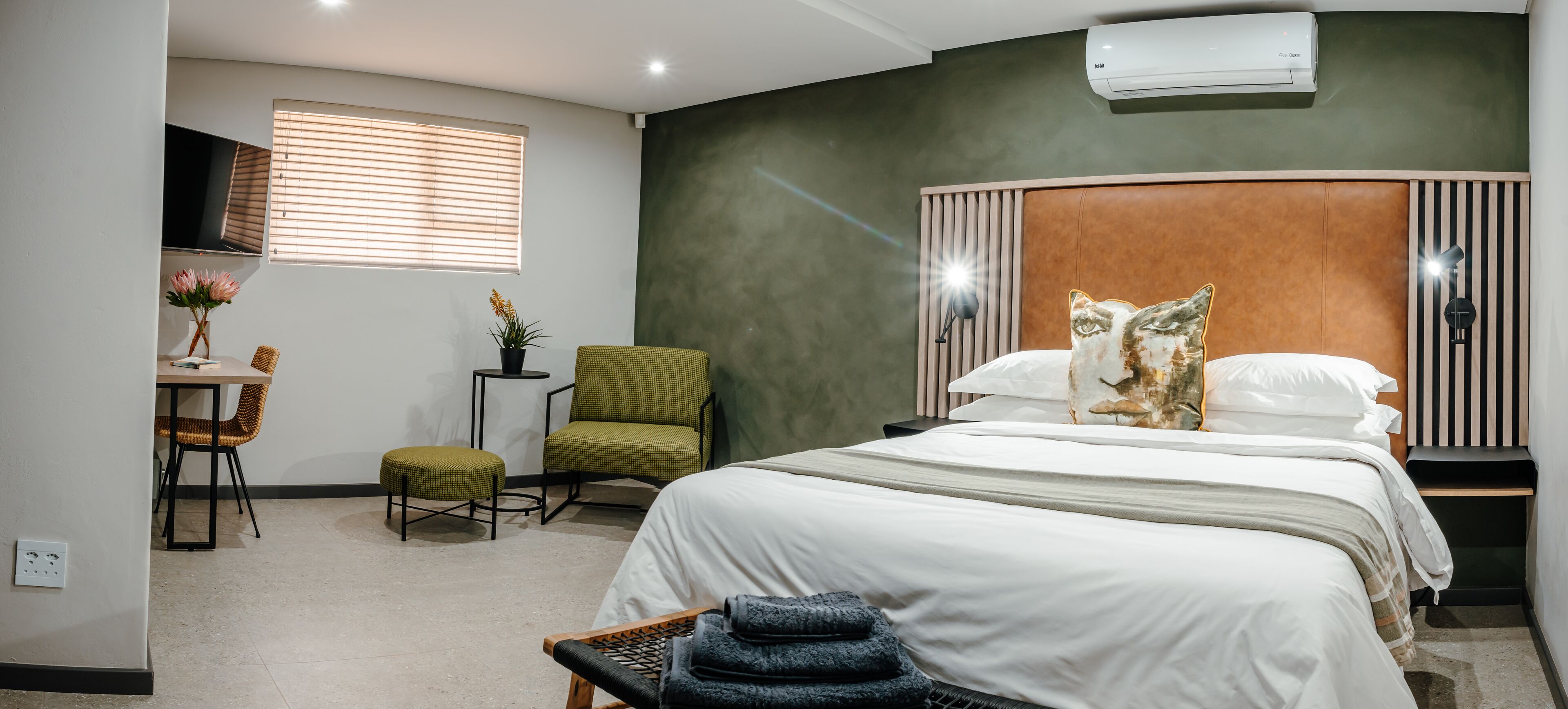 Ein Hotelzimmer mit Bett, Schreibtisch mit Stuhl, einem kleinen Tisch mit Pflanze und einem an der Wand befestigten Fernseher.