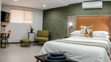 Ein Hotelzimmer mit Bett, Schreibtisch mit Stuhl, einem kleinen Tisch mit Pflanze und einem an der Wand befestigten Fernseher.
