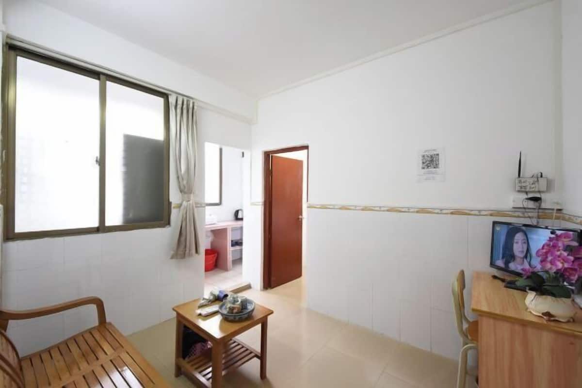 A room with a wooden desk, a television, a window with curtains, and a door leading to another room.