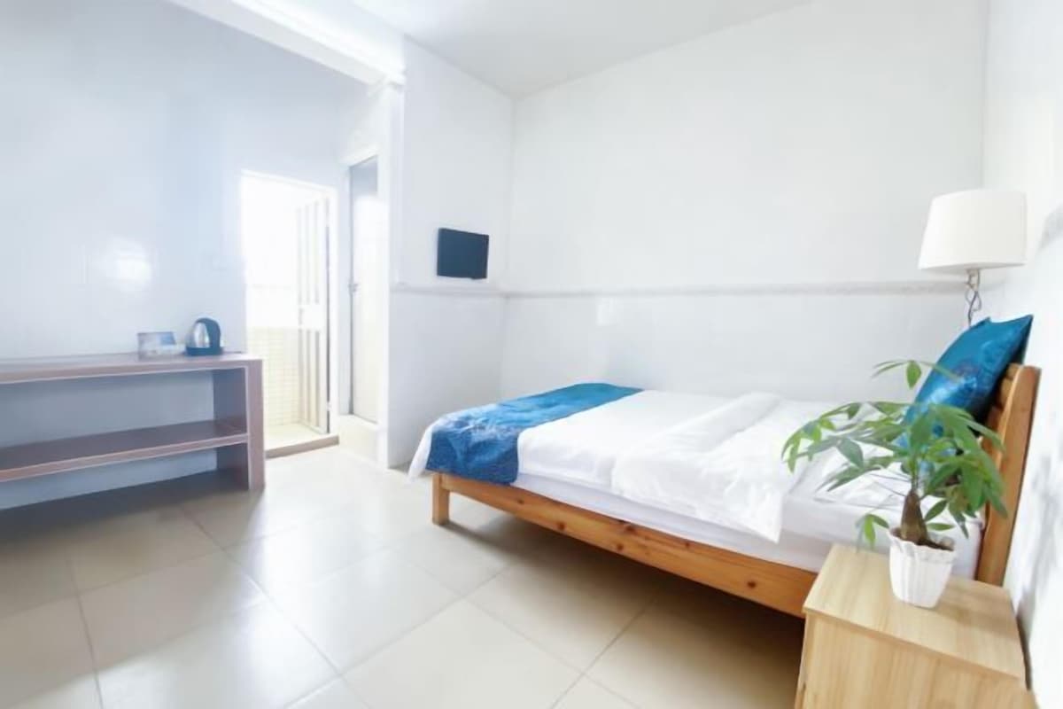A bedroom with a bed, bedside table, and a potted plant.