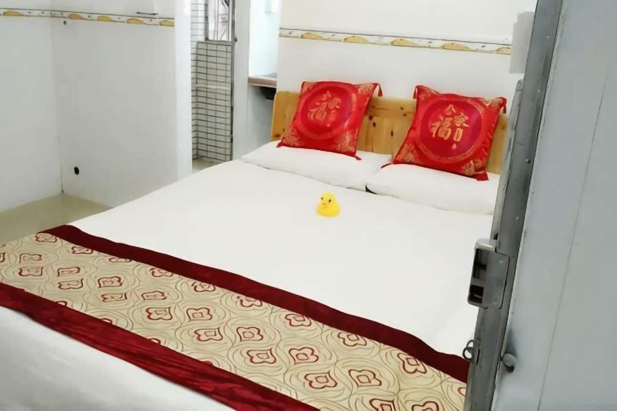 A bed with a patterned bedspread, two red pillows, and a small yellow object on the bed.