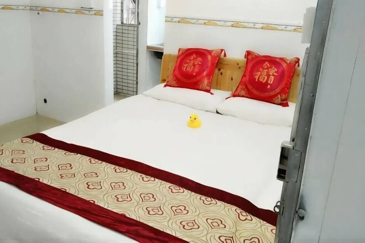 A bed with a patterned bedspread, two red pillows, and a small yellow object on the bed.