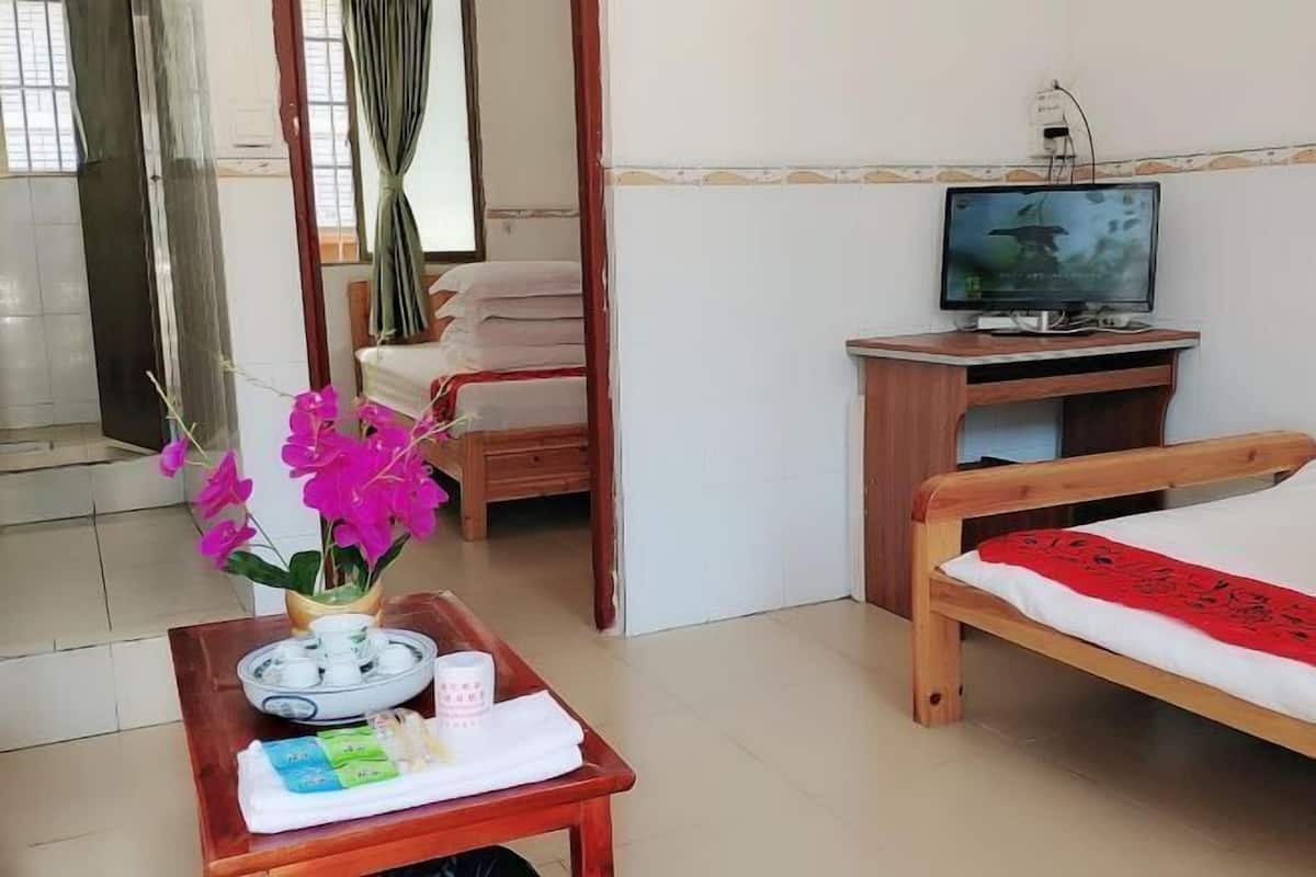 A hotel room with a bed, a wooden desk with a television, a small table with toiletries, and a window with curtains.