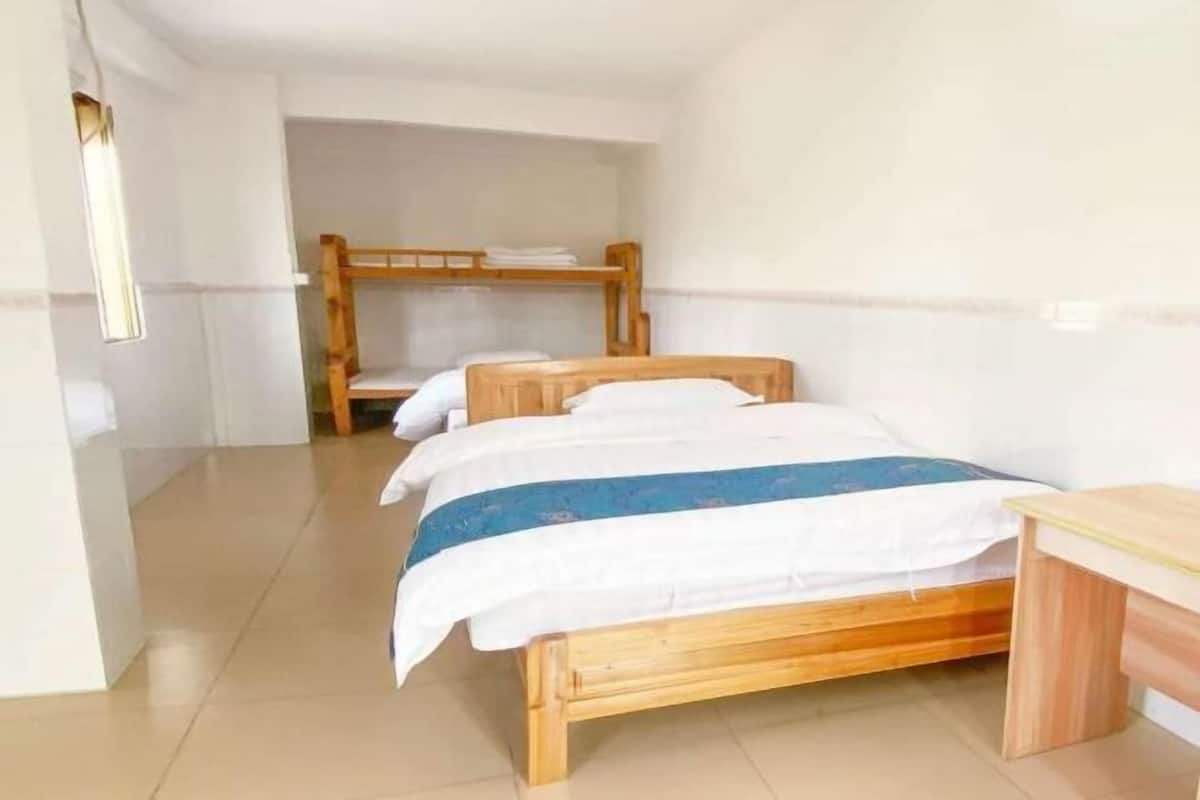 A room with two wooden beds, a small wooden table, and a bunk bed in the background.