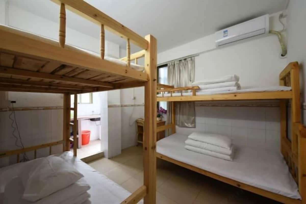 A dormitory room with two bunk beds, a window with curtains, and an air conditioning unit on the wall.