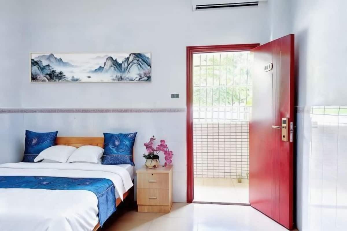 A bedroom with a bed, a nightstand, a red door, and a wall-mounted painting.