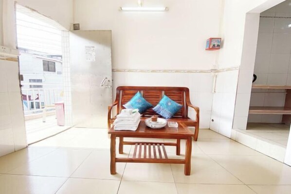 Quarto com um banco de madeira, duas almofadas azuis, uma toalha branca e uma pequena mesa com xícara e pires.