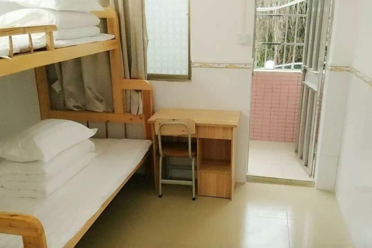 A dormitory room with bunk beds, a desk, and a chair.