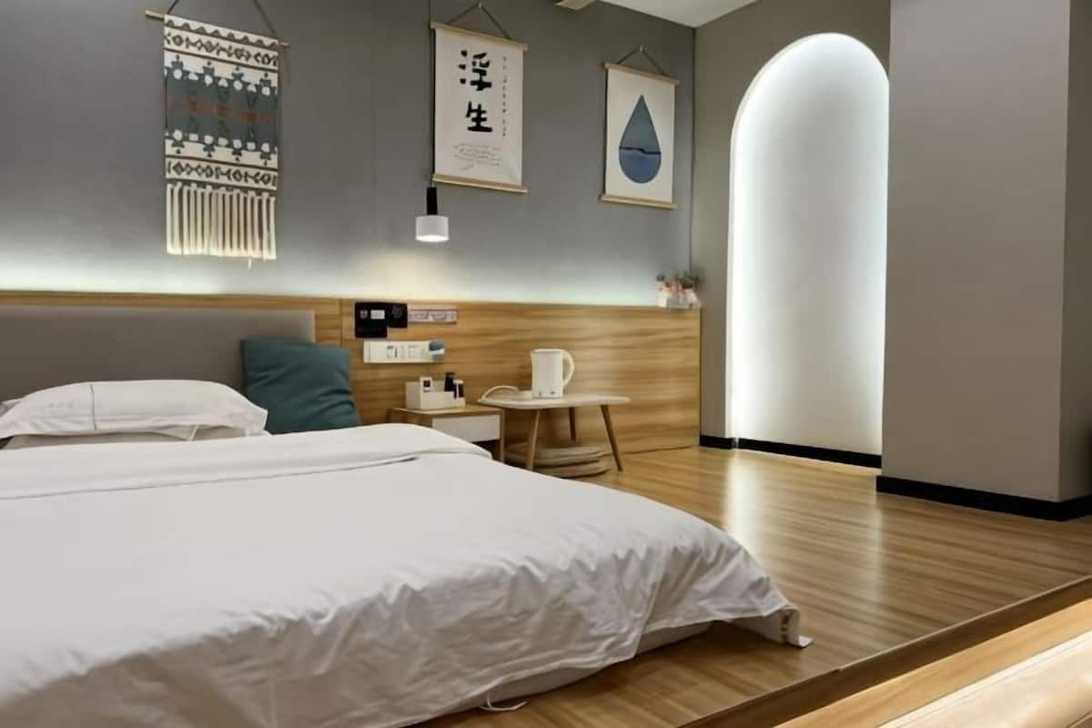 A modern hotel room with a large bed, bedside table, and a small table with a lamp.