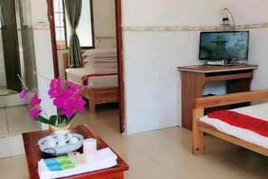 A hotel room with a bed, a TV on a wooden stand, a small table with a tray, a window with curtains, and a wooden door.
