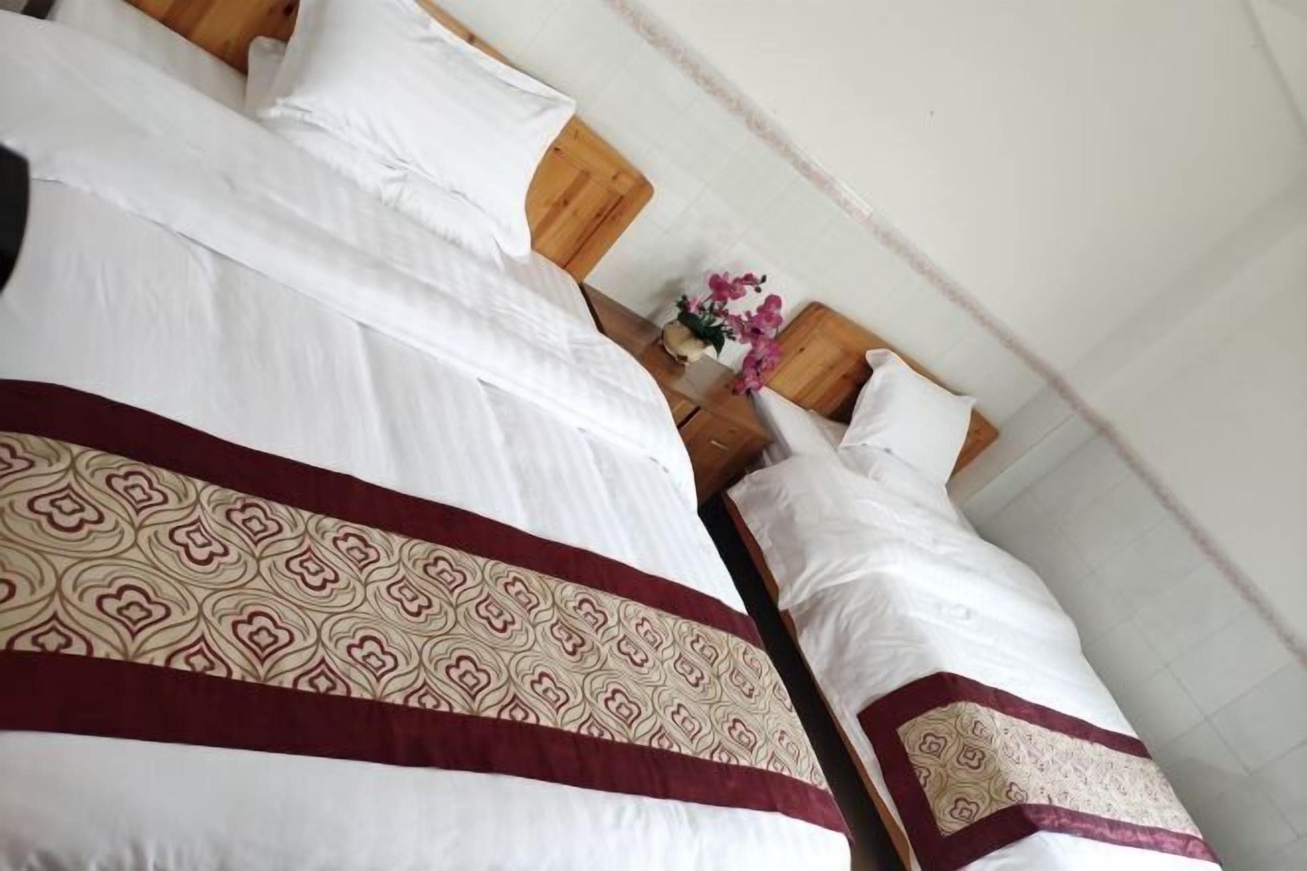 A hotel room with a large bed, wooden headboard, and a vase with flowers.