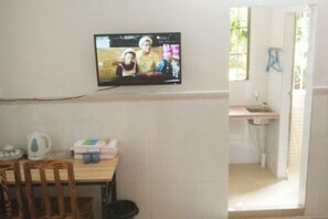 Ein Zimmer mit Fernseher an der Wand, einem Tisch mit Stühlen, einer Küchenzeile inklusive Spüle und einem Fenster.