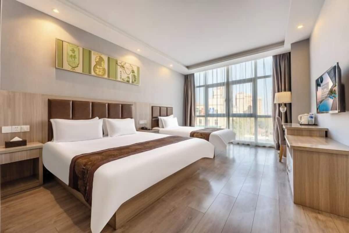 Habitación de hotel con dos camas, un escritorio y un ventanal con vistas a la ciudad.