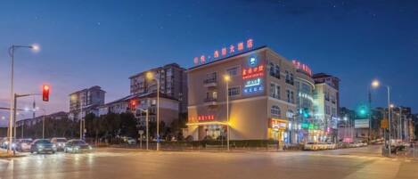 A multi-story hotel with illuminated signage, a flat roof, and a street view.