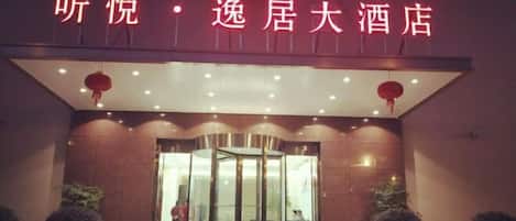 A hotel entrance with a revolving door, a red neon sign, and potted plants.