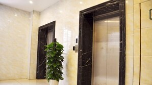 An elevator area with marble walls, a potted plant, and two elevators. - Tingyue Yiju Hotel (Shanghai)