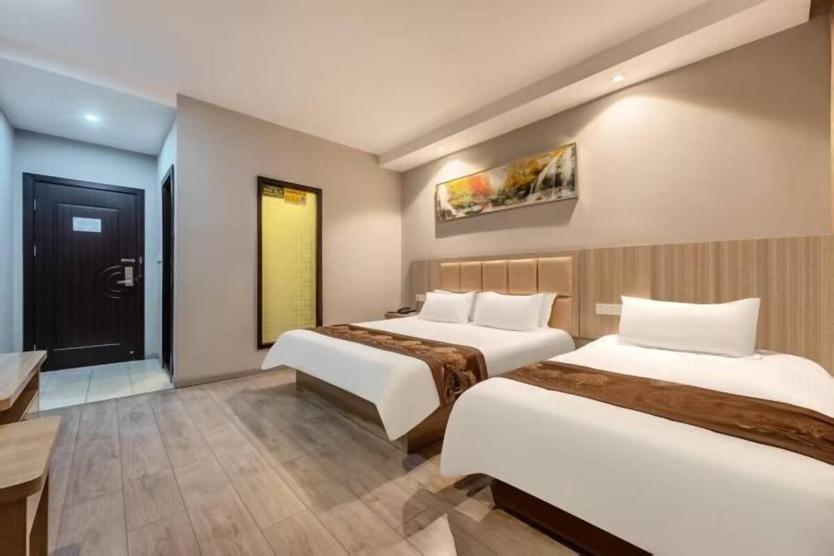 Habitación de hotel con dos camas, un escritorio, una puerta y un cuadro en la pared.