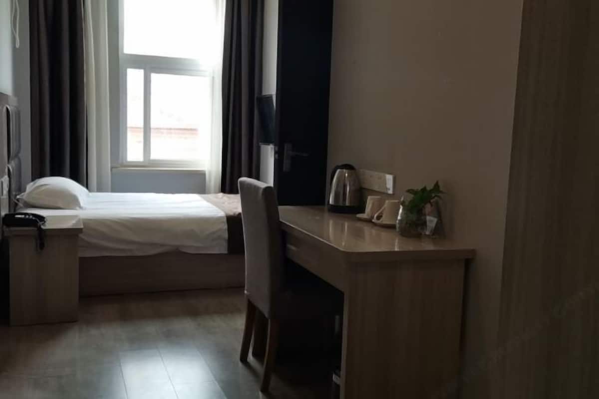Habitación de hotel con una cama, un escritorio, una silla, una mesita con una planta, una tetera y un teléfono.