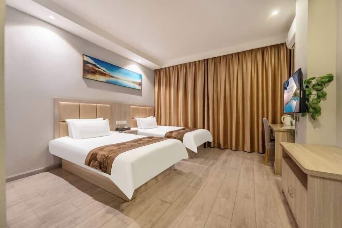 Una habitación de hotel con dos camas, televisión, escritorio y un ventanal con cortinas.