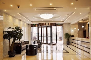 A lobby with a reception desk, seating area, large potted plants, and a glass door entrance.