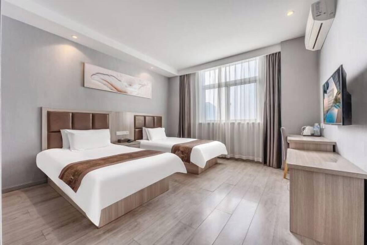 Habitación de hotel con dos camas, un escritorio, un televisor y un ventanal grande con cortinas.