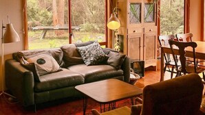 A cozy living room with a leather sofa, a dining table, and a wooden ceiling. - Birdsong - a cosy cabin with a view (Adventure Bay)