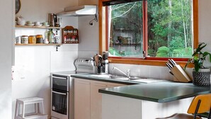 A kitchen with wooden beams, a large window, and a hanging light fixture. - Birdsong - a cosy cabin with a view (Adventure Bay)