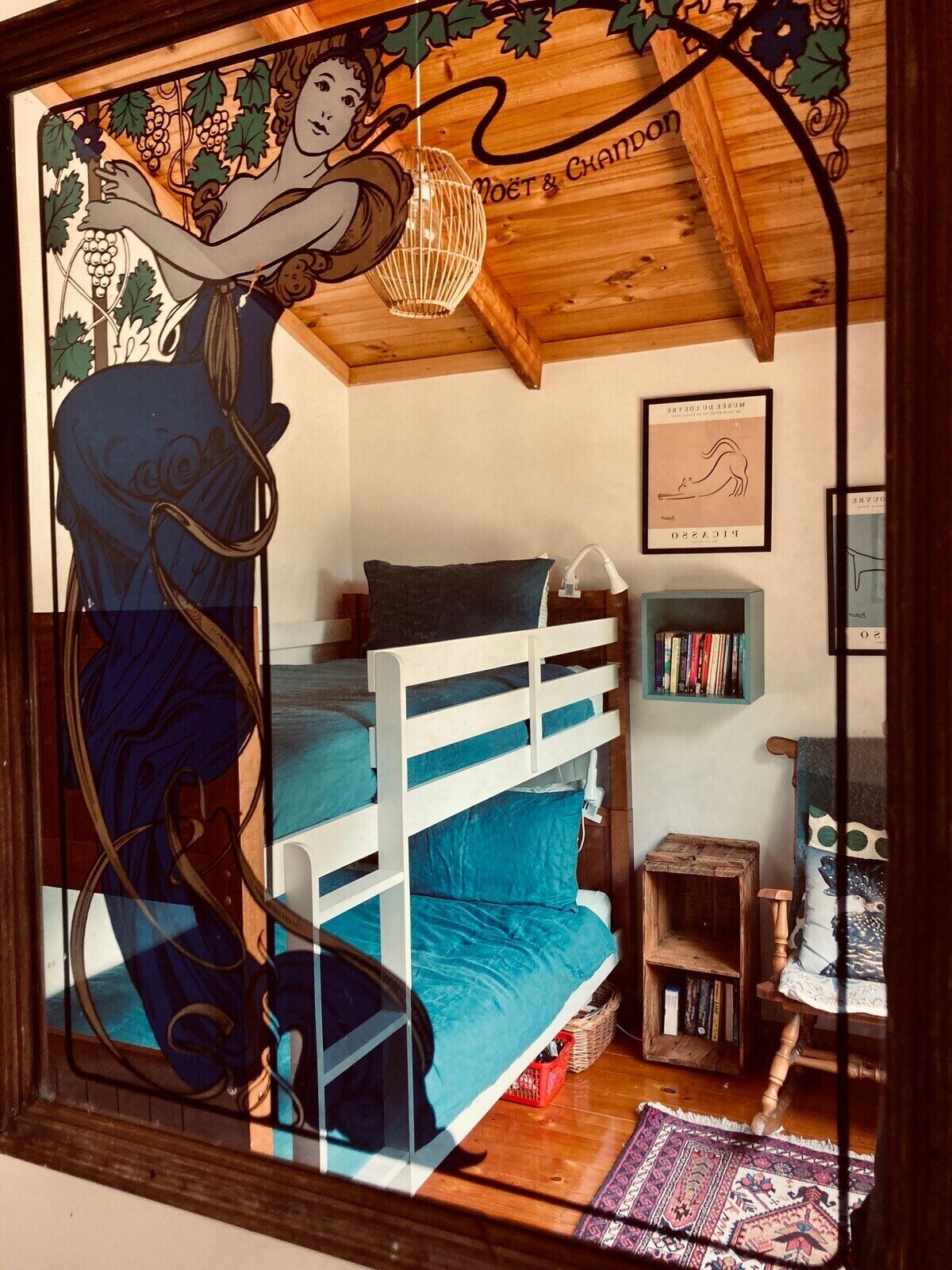 Une chambre avec un lit superposé, un plafond en bois, un mur orné de tableaux encadrés et une fenêtre décorée de vitraux.