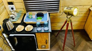 Una cuineta compacta amb fogó, bullidor i una taula petita amb tasses i pots.