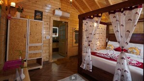 Habitació de tipus cabana de fusta, amb un llit, un armari de fusta i una taula petita amb un ram.