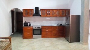 A compact kitchen with wooden cabinets, a stove, a sink, and a refrigerator. - Orchid Dream (Bentota)
