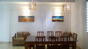A dining area with a long table and chairs, two hanging light fixtures, and two framed paintings on the walls. - Orchid Dream (Bentota)