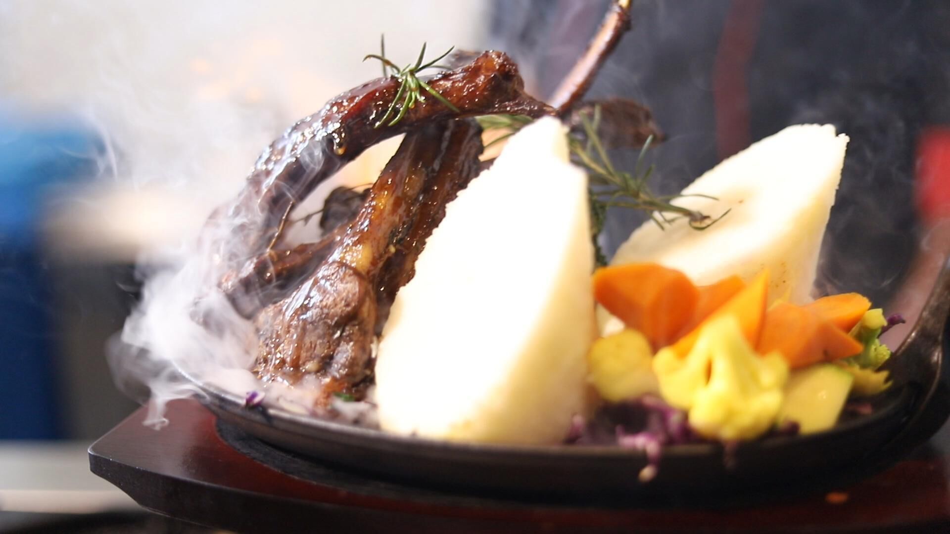 Une assiette comprenant un jarret d’agneau rôti, des pommes de terre bouillies et un accompagnement de légumes variés.