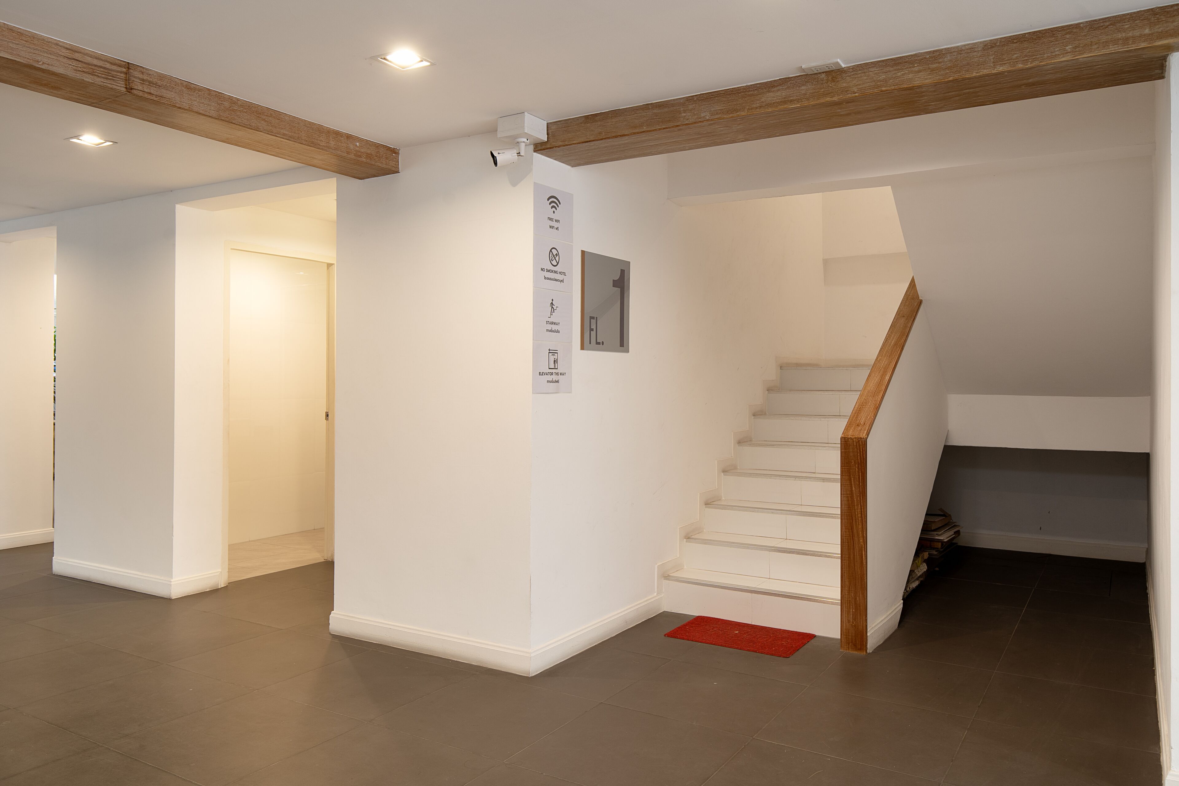 A spacious interior with a staircase, white walls, and a wooden beam ceiling.