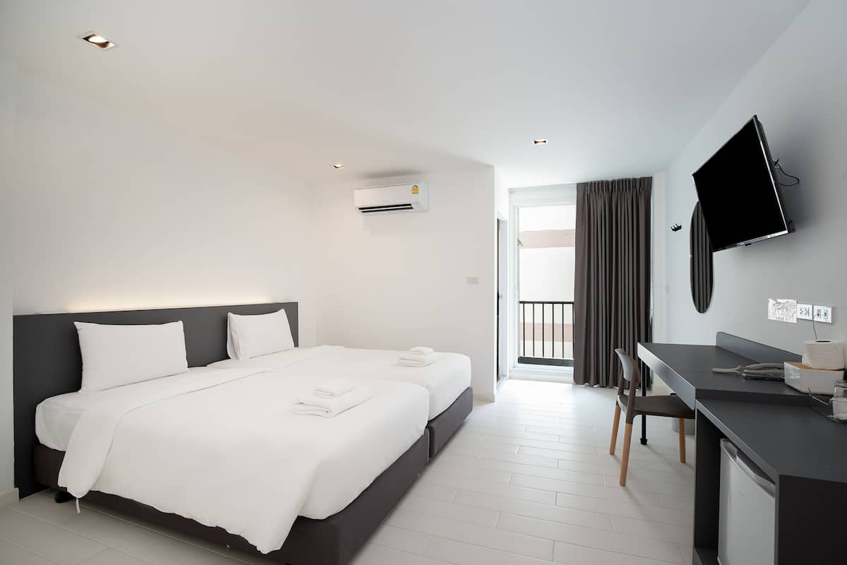 A modern hotel room with a large bed, a desk, a flat-screen TV, and an air conditioning unit.
