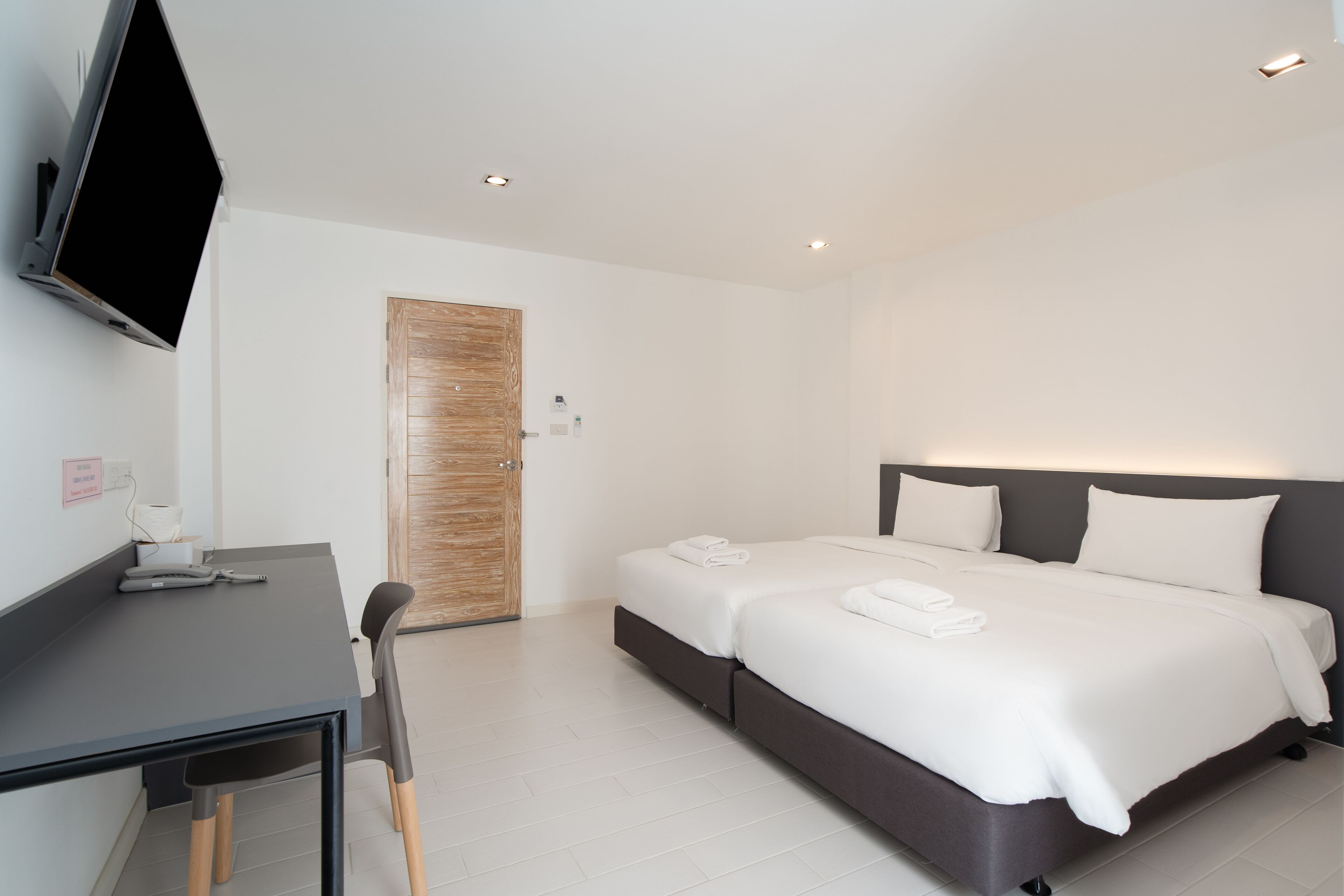 Une chambre d’hôtel moderne équipée d’un lit, d’une table de chevet, d’une chaise et d’un téléviseur à écran plat fixé au mur.