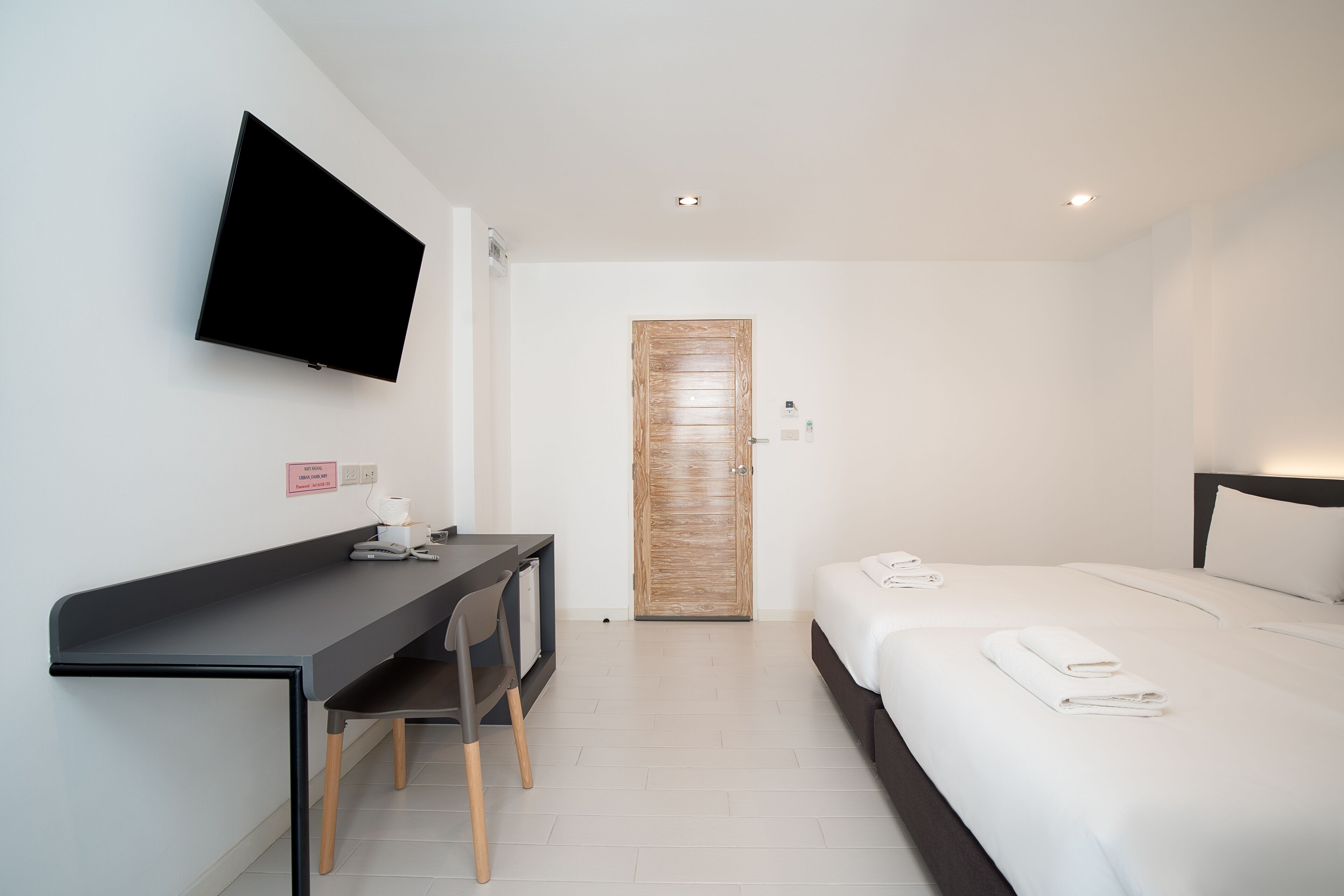 Ein Hotelzimmer mit Bett, Schreibtisch mit Stuhl, Wandfernseher und einer Holztür.