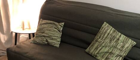 A dark green sofa with two patterned pillows, positioned against a white wall.