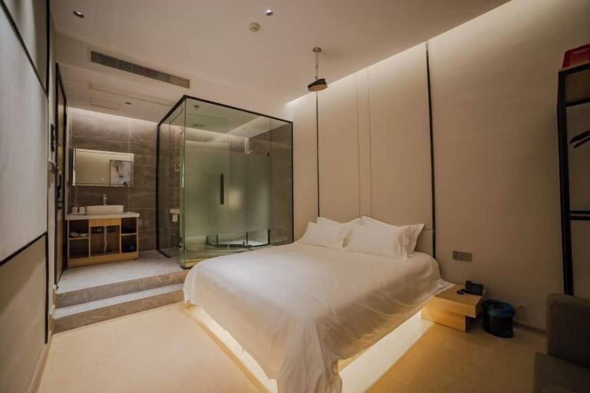 Un dormitorio moderno con cabina de ducha de vidrio, una cama con ropa de cama blanca y una mesita de noche.