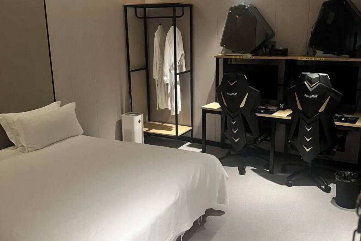 Una habitación de hotel con una cama, dos sillas de gaming, un escritorio y un perchero.