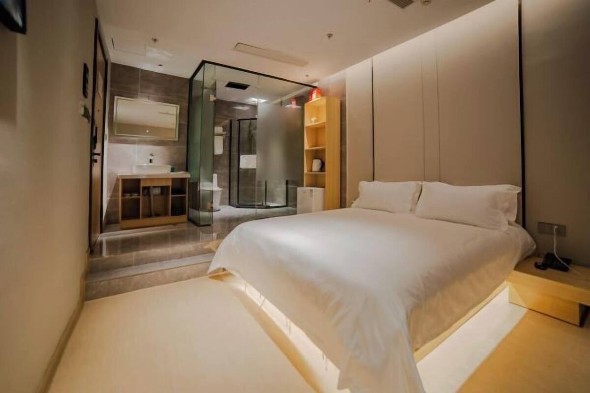 Un dormitorio moderno con una cama grande, cabina de ducha de vidrio y una mesita de noche de madera.