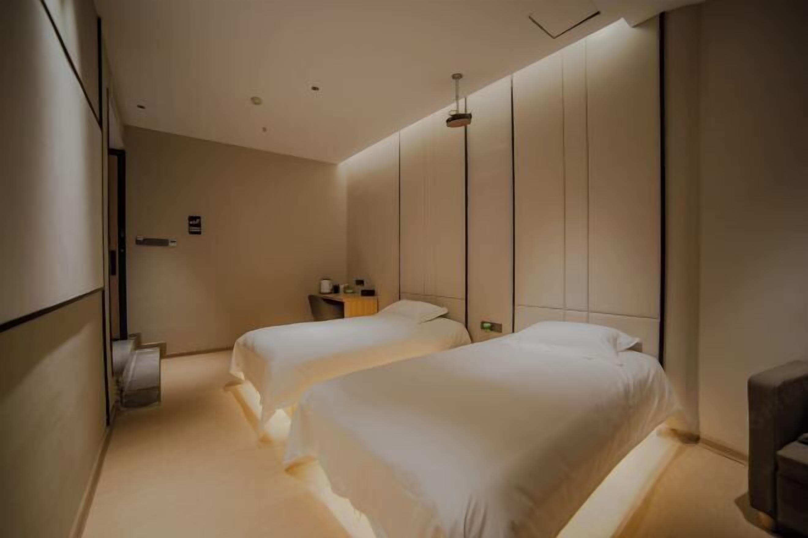 A modern hotel room with two beds, a small seating area, and a minimalist design.