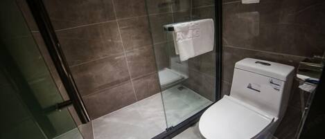 A modern bathroom with a glass-enclosed shower, a white toilet, and a visible trash bin.