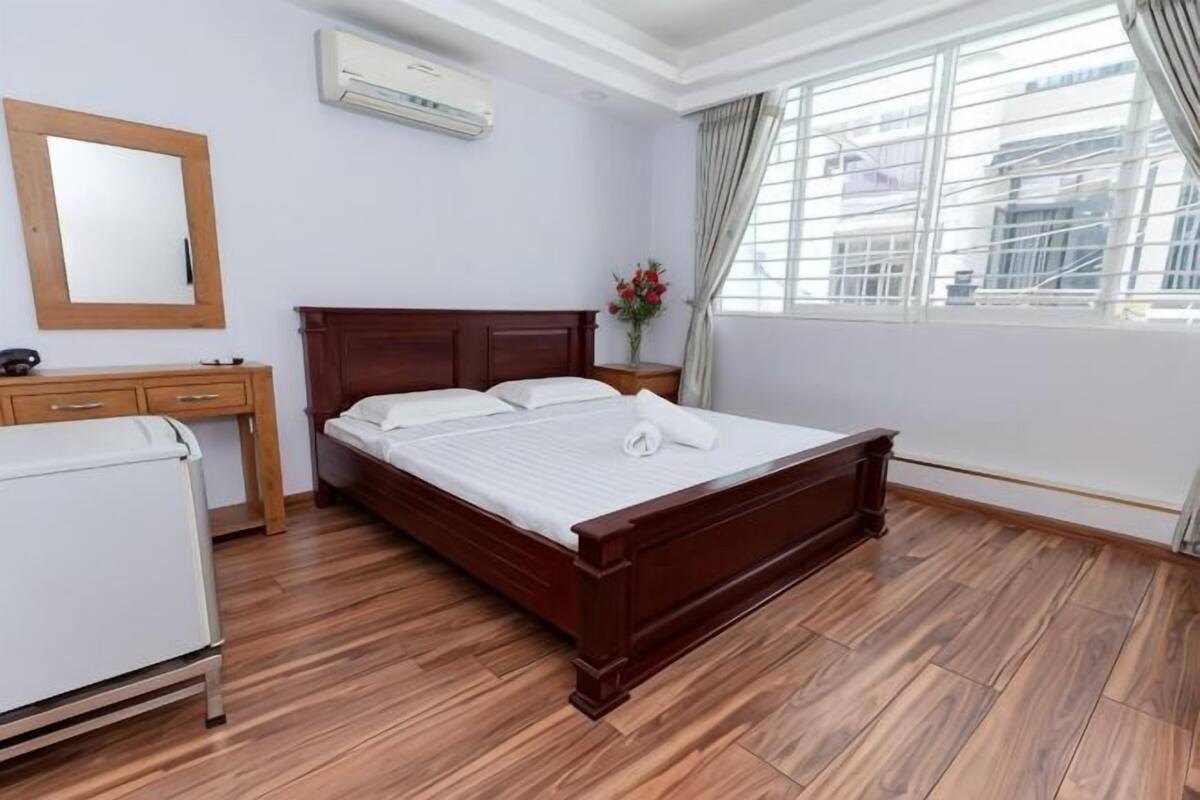 Ein Schlafzimmer mit einem hölzernen Bett, einem Schreibtisch, einem Stuhl, einem Spiegel und einem Fenster mit Vorhängen.